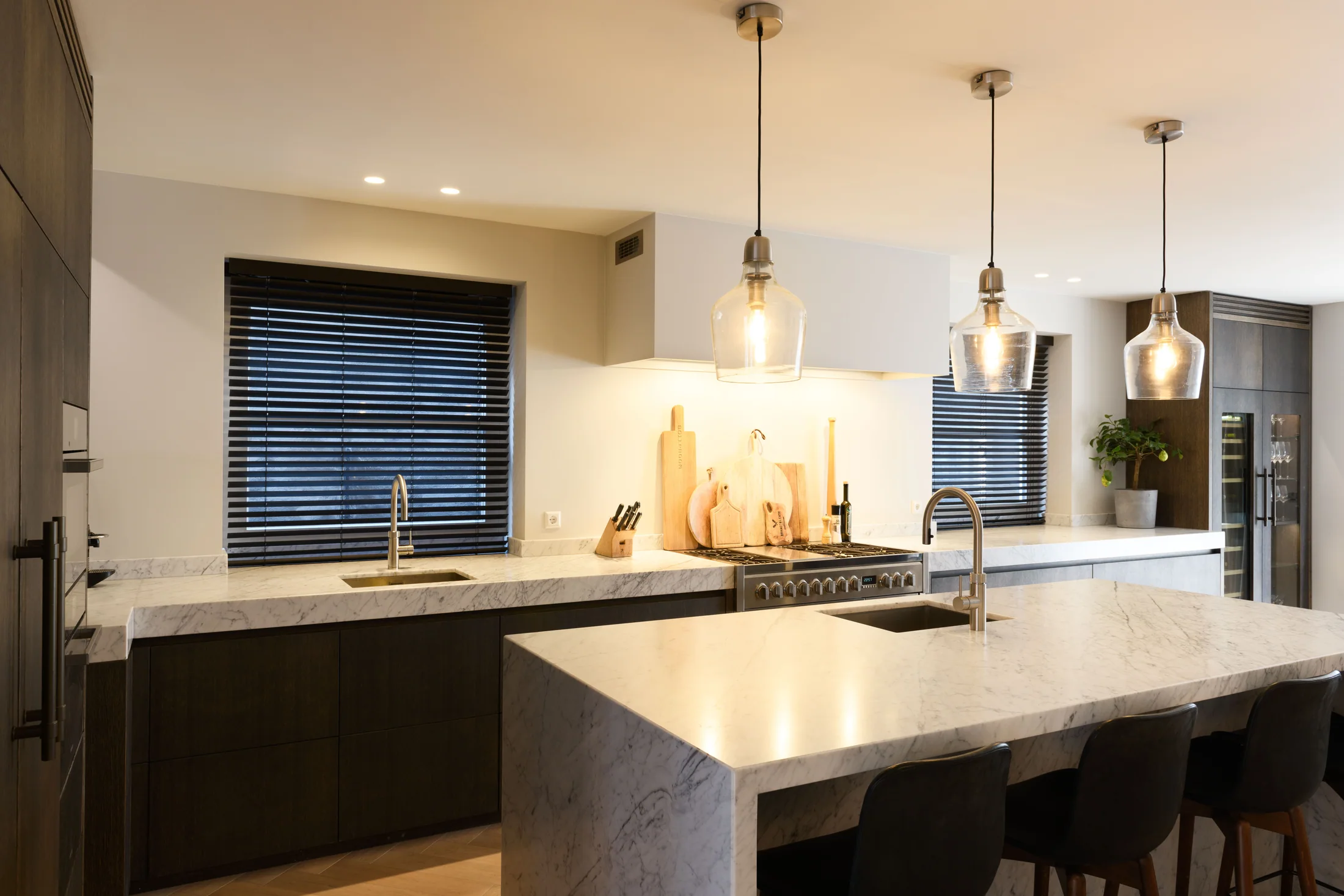 Licht marmeren eiland met donkere kasten en glazen hanglampen