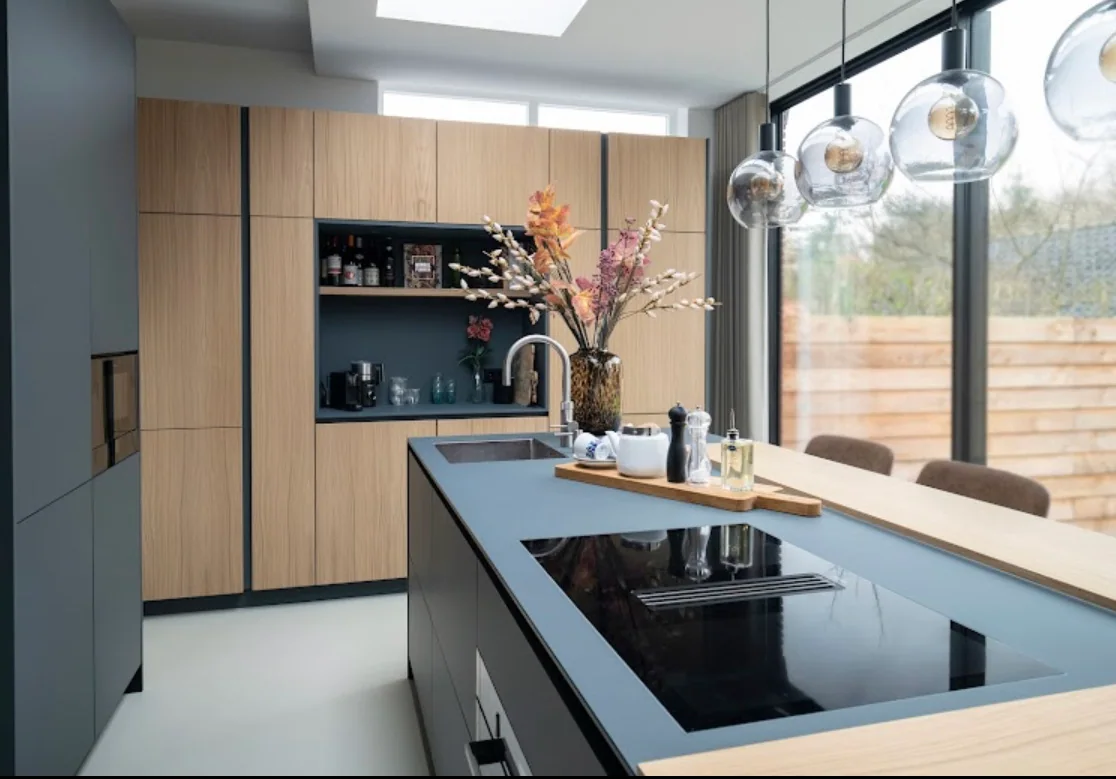 Licht houten kasten, een donker kookeiland en glazen hanglampen in de keuken van Ellen Kok