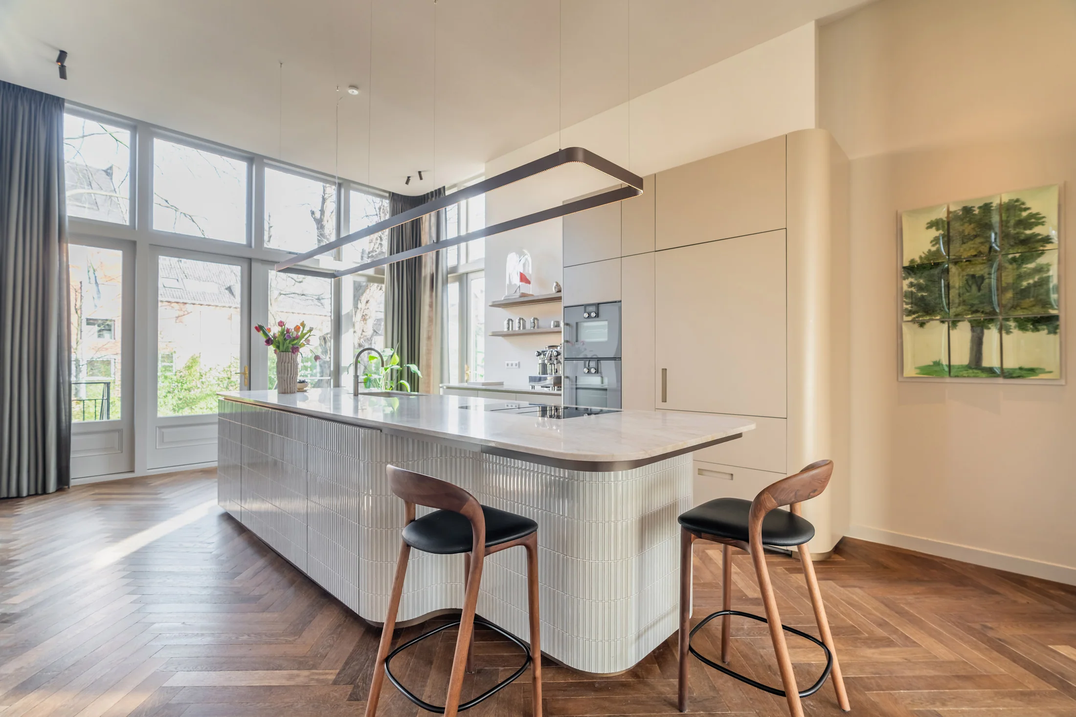 Licht afgerond kookeiland met Yuki-tegels naast hoge ramen